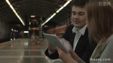 一对年轻的<strong>情侣</strong>在地铁站等车，他们一边用平板电脑看东西一边讨论